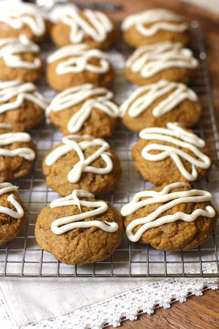 A side shot of iced pumpkin cookies on a wire baking rack, on white napkin.