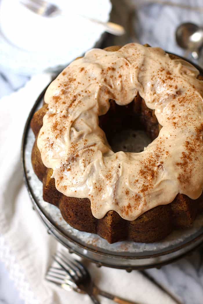 Overhead shot of a pumpkin bundt cake with cinnamon icing, on a gray cake platter with white napkin beside it.