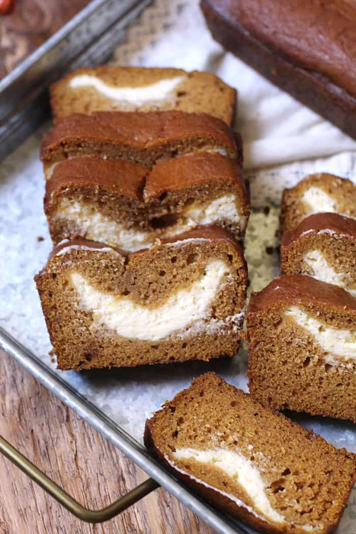 Overhead shot of sliced pumpkin bread with big layers of cream cheese in the middle of the bread, all on a gray tray.