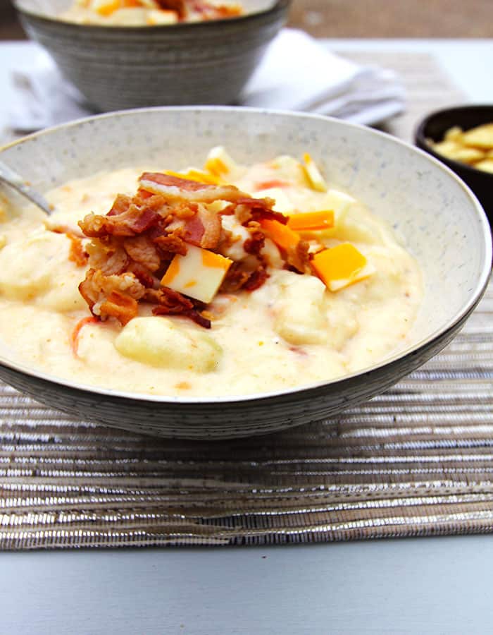 Side shot of a bowl of chunky loaded potato soup, with bacon on top.