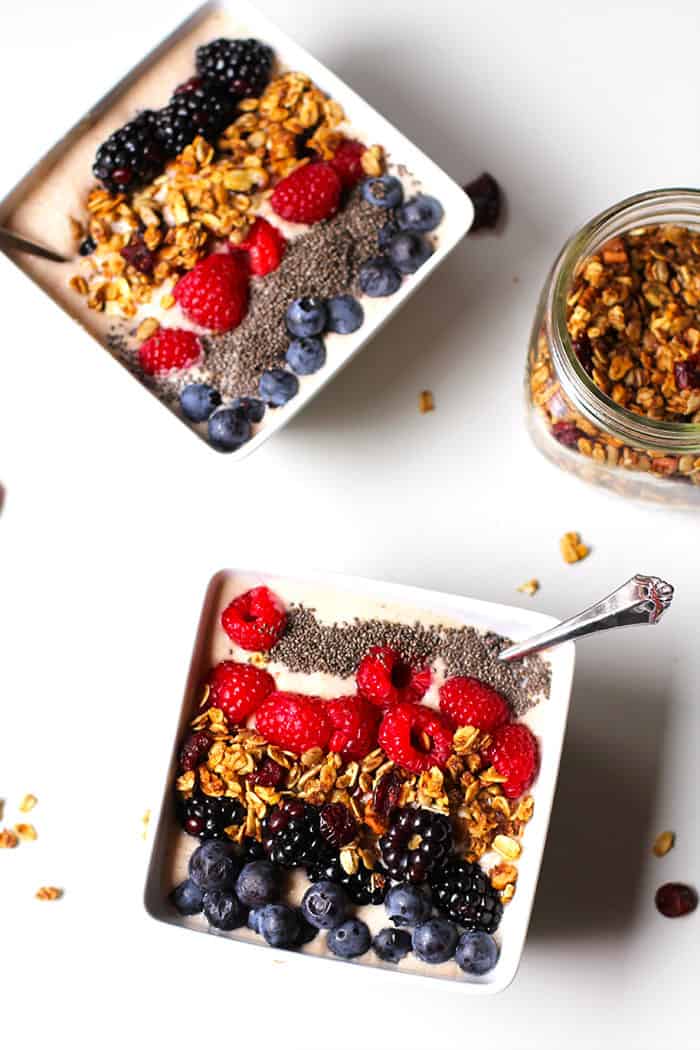 Overhead shot of two Acai Smoothie Bowls with spoons inside, and a jar of granola.