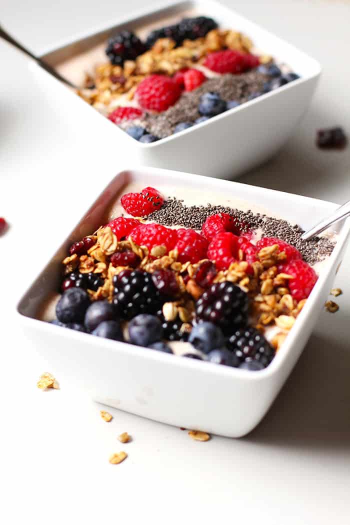 Side shot of two square bowls of Acai Smoothies, with fruit on top.