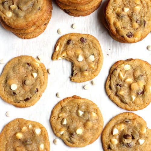 Overhead shot of a bunch of chocolate chip cookies on white parchment paper, with a bite out of one of them.
