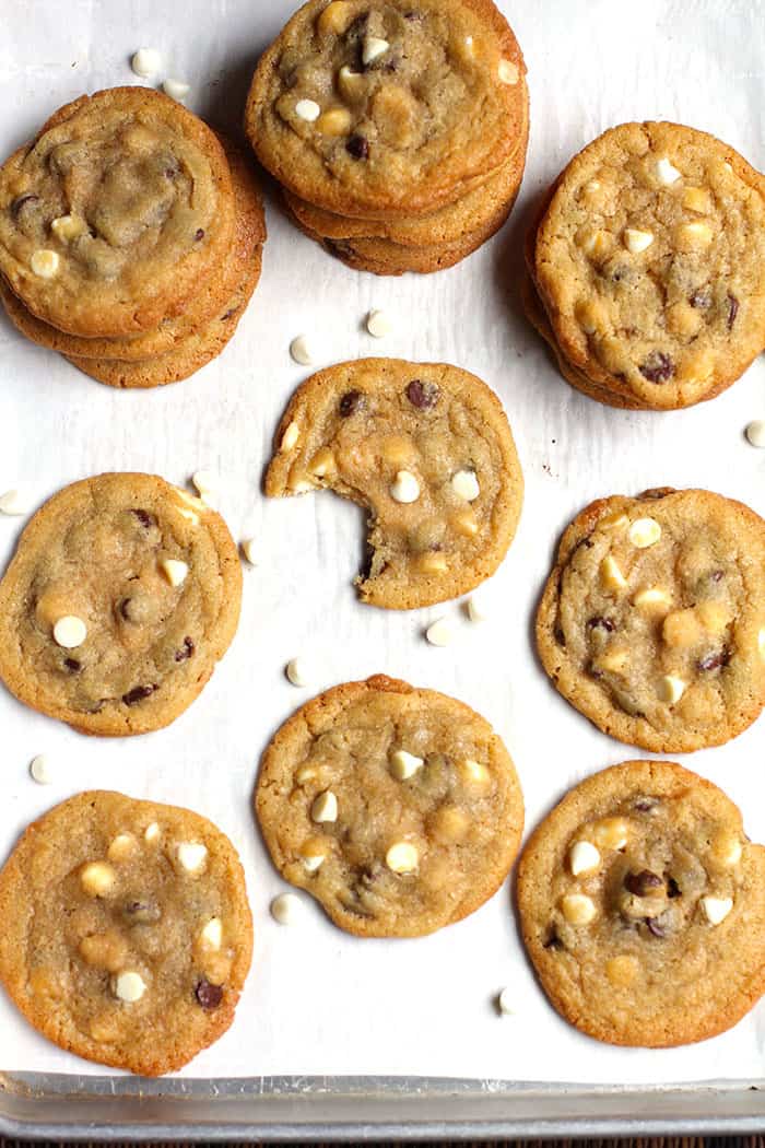 Overhead shot of a bunch of chocolate chip cookies on white parchment paper, with a bite out of one of them.
