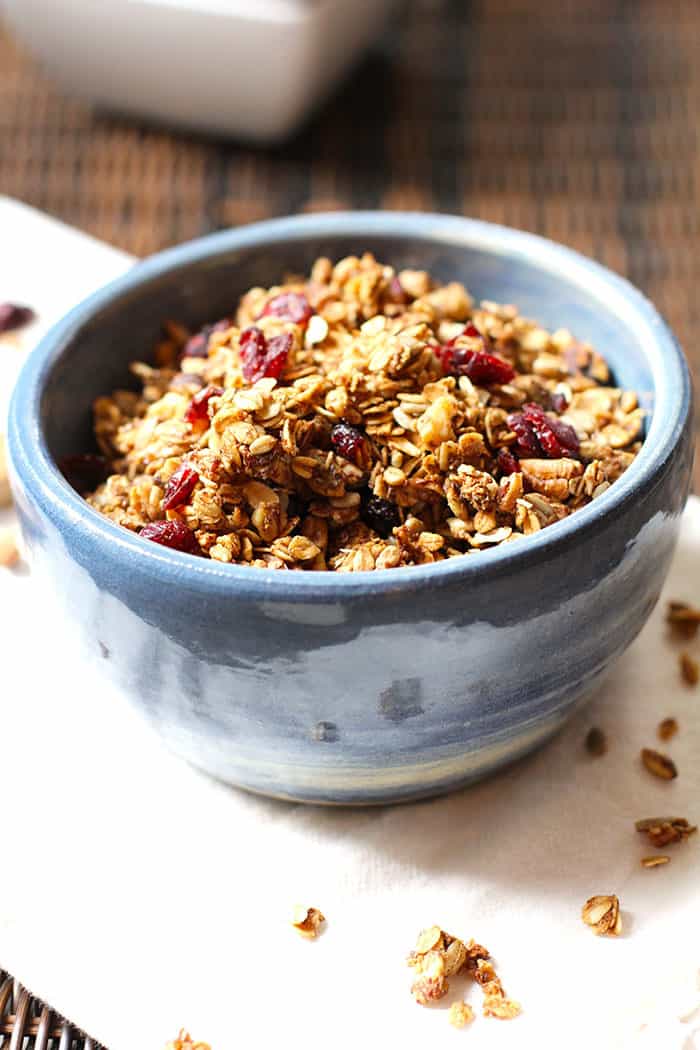 Side shot of a round blue bowl, filled with granola, on a wicker tray.