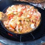 Shot of a big pan of paella on a grill, with some tin foil being lifted off.