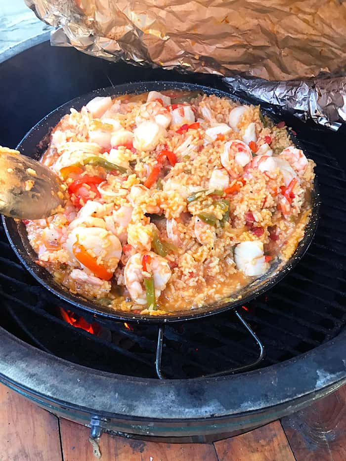 Shot of a big pan of paella on a grill, with some tin foil being lifted off.