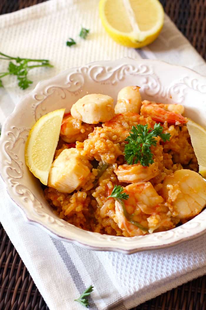 A white bowl filled with shrimp and scallops paella, on a white napkin.