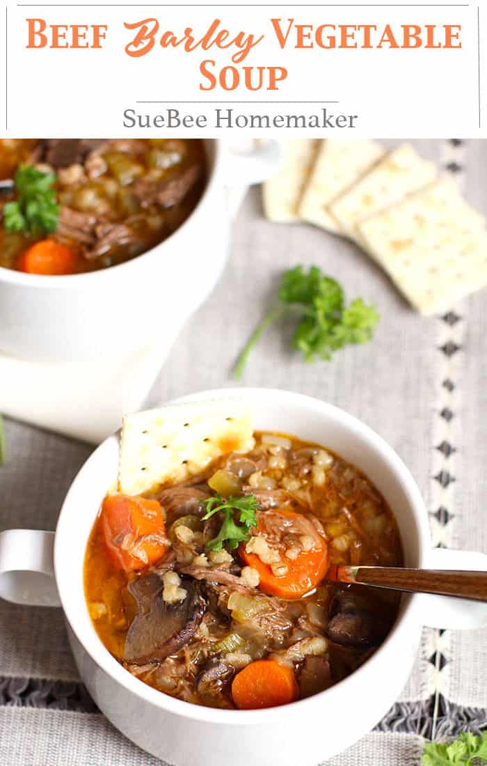 A closeup on a white bowl of beef barley vegetable soup, with a spoon in it.