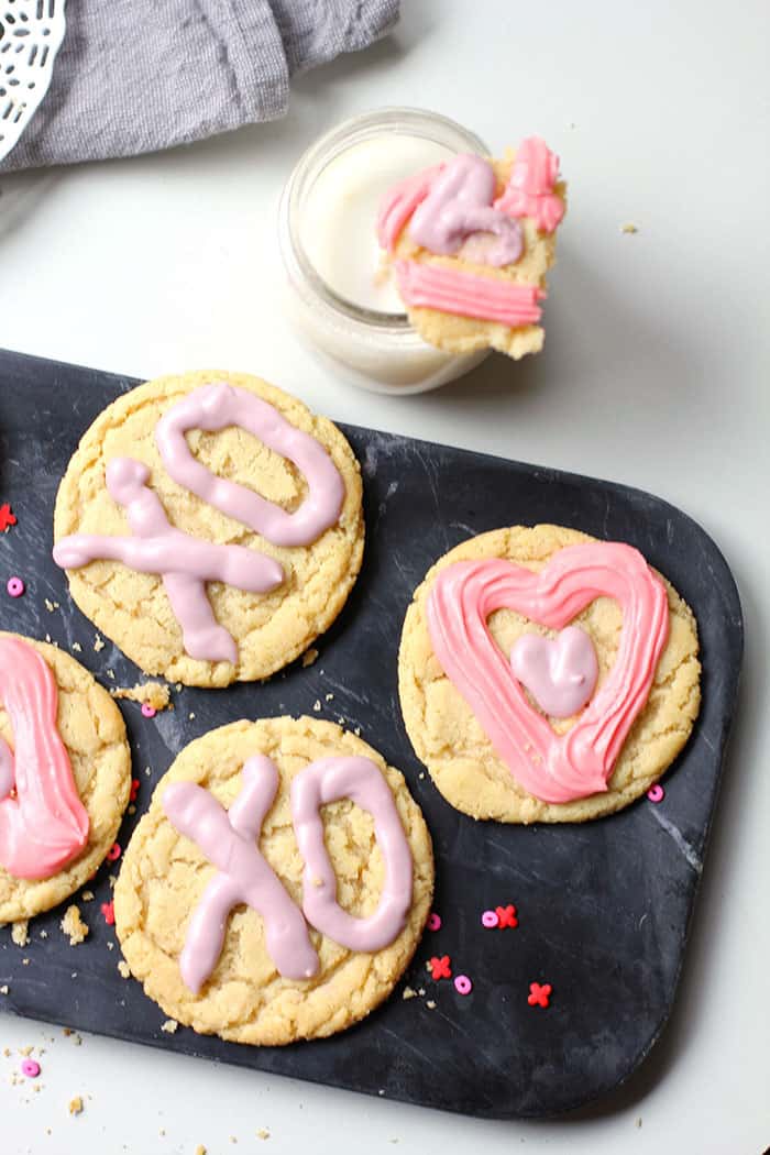Four chewy sugar cookies on a black tray with a jar of milk.
