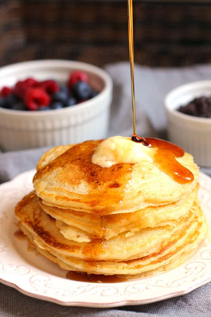 A stack of buttermilk pancakes with butter on top and a big drizzle of syrup hitting the top.