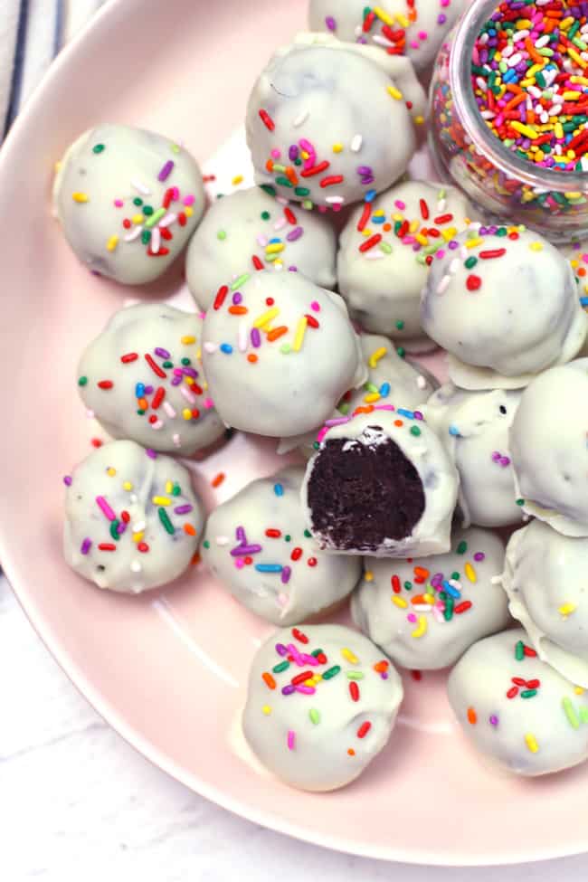 Overhead shot of a pink bowl of white chocolate Oreo Truffles, with a bowl of sprinkles.