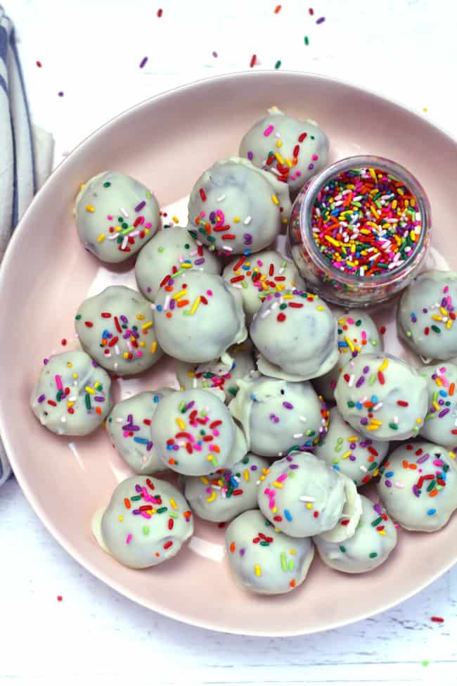 Overhead shot of a pink bowl of white chocolate Oreo Truffles, with sprinkles on a white background.
