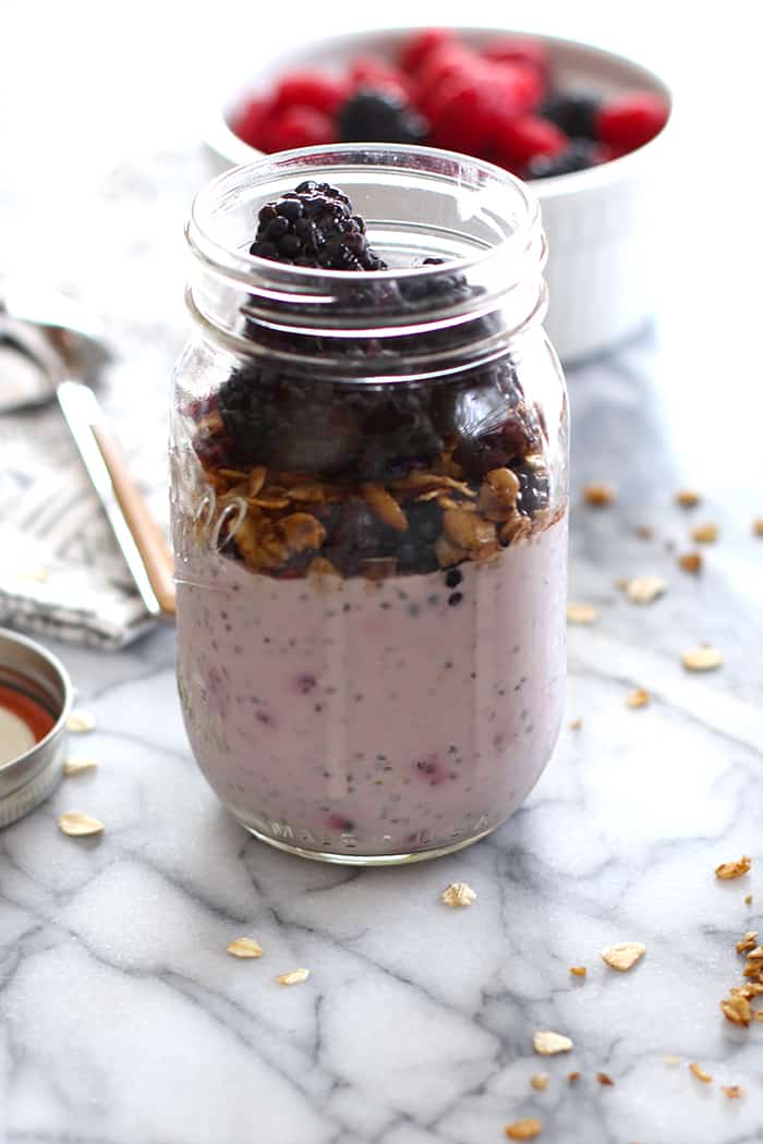 Side view of mason jar filled with berry chia overnight oats, and granola and fruit.