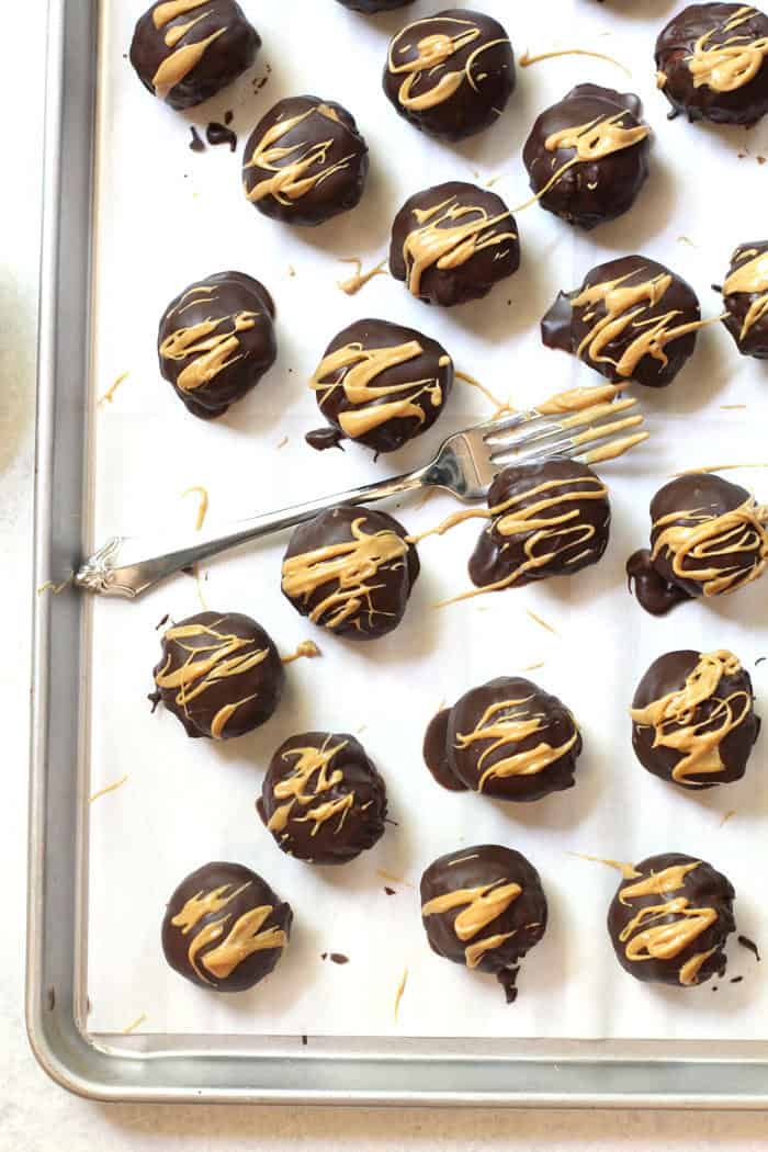 Overhead shot of cookie balls that were just drizzled with peanut butter, a fork lying in the middle of them on a sheet pan.
