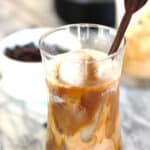 A glass of cold brew coffee, with milk and a stir stick.