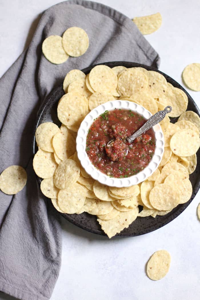 Overhead shot of a small white bowl of homemade salsa, on a plate with Tostito chips.