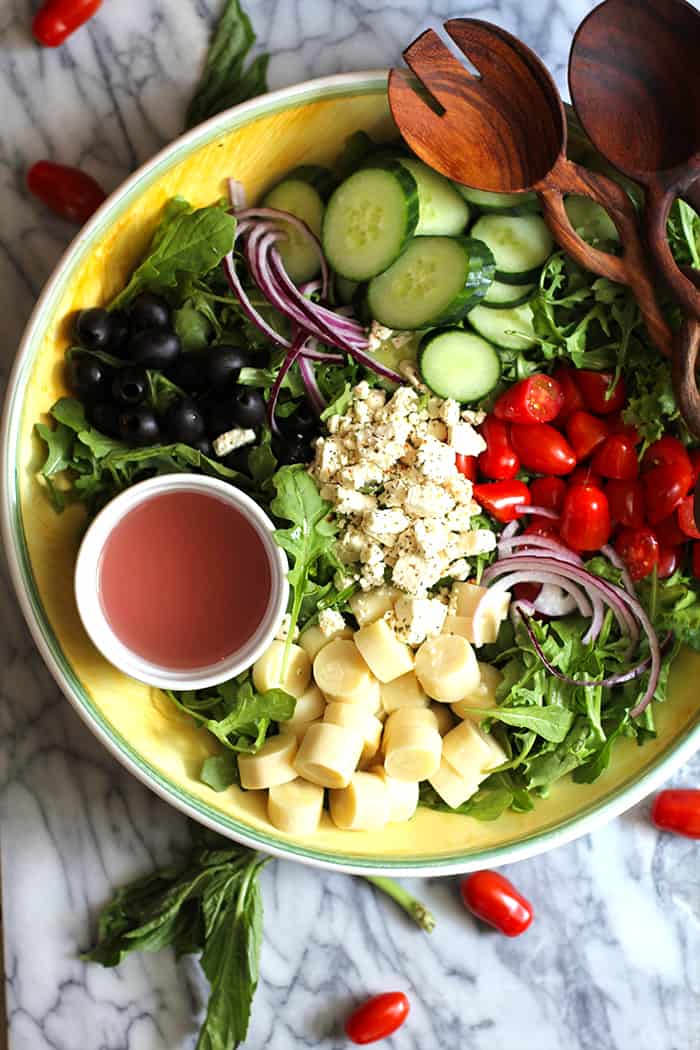 Overhead shot of a large bowl of Italian Hearts of Palm Salad, with ingredients in sections and two wooden spoons.