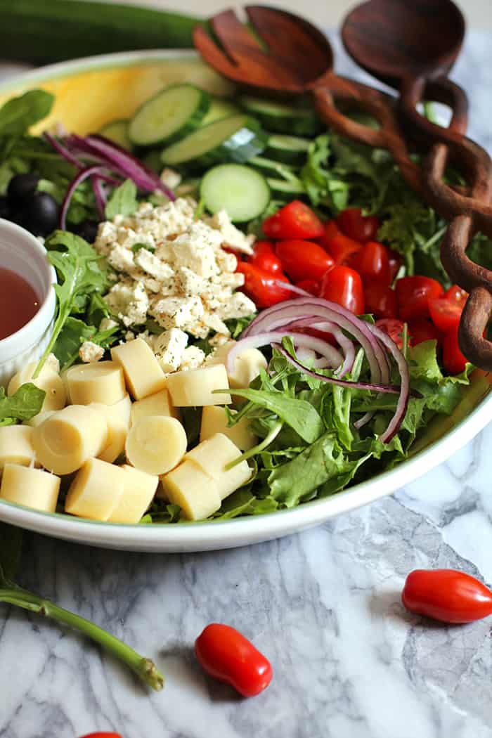 Side view of a large bowl of Italian Hearts of Palm Salad, with ingredients in sections and two wooden spoons.