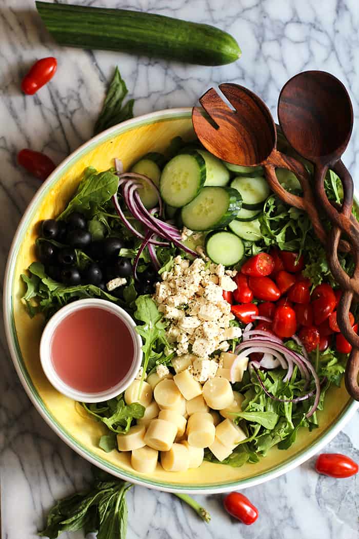 Overhead shot of a large bowl of Italian Hearts of Palm Salad, with ingredients in sections and two wooden spoons.