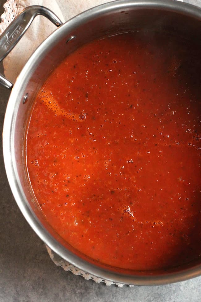 Overhead shot of a large pot of homemade tomato soup, on a gray background.