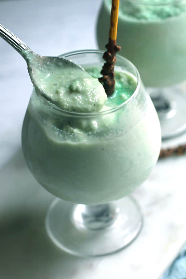 Side shot of two glasses of frozen grasshopper drinks, with a spoonful showing.
