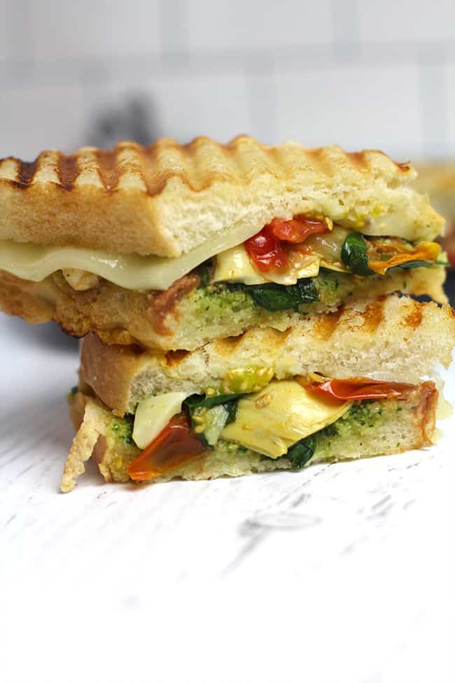 Side shot of a stack of two roasted vegetable pesto paninis, on a white background.