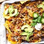 Overhead shot of a half of a sheet pan of beef and bean nachos, with toppings.