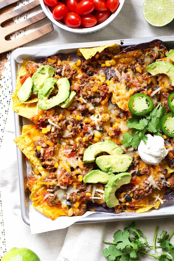 Overhead shot of a half of a sheet pan of beef and bean nachos, with toppings.