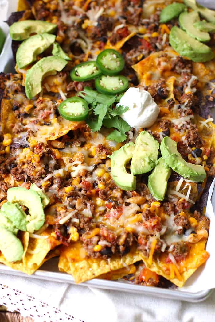 Side shot of a sheet pan of beef and bean nachos, loaded with toppings.