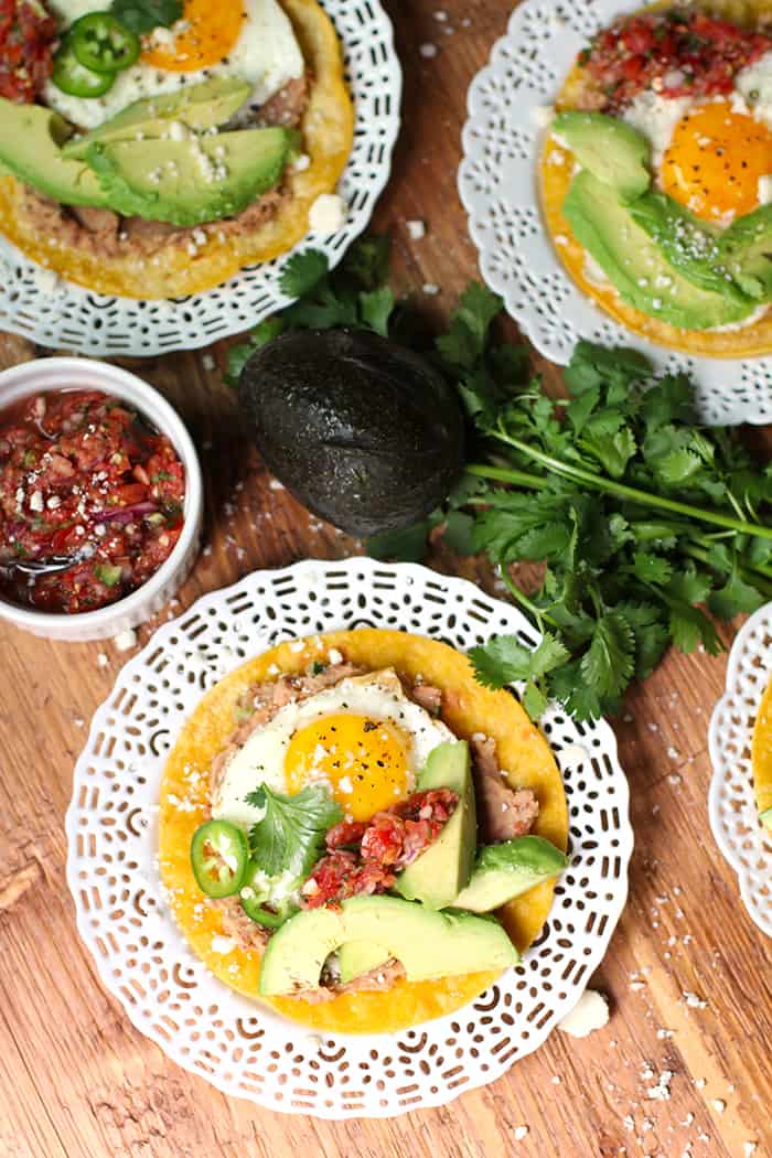 Overhead shot of several plates of Huevos Rancheros Tostadas, on a wooden board.