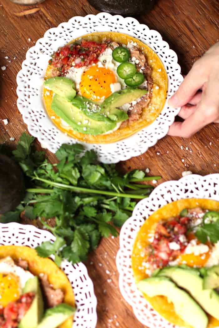 One hand on a white plate with a tostada on top.