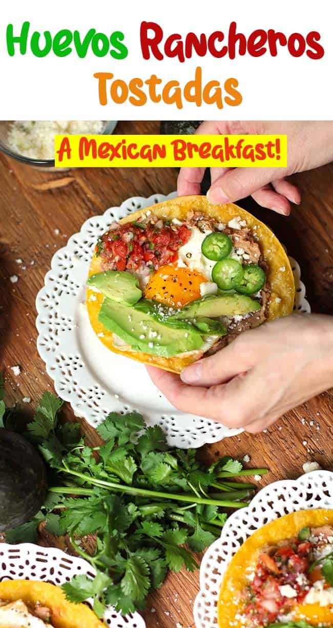 Hands picking up a huevos rancheros breakfast tostada from a white plate.