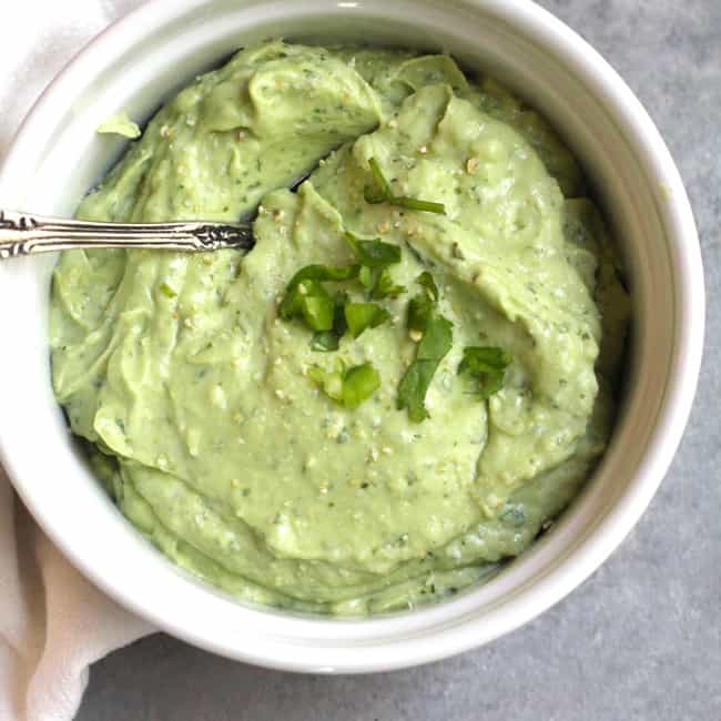 Overhead shot of a small white bowl with Avocado Crema, and a spoon inside.