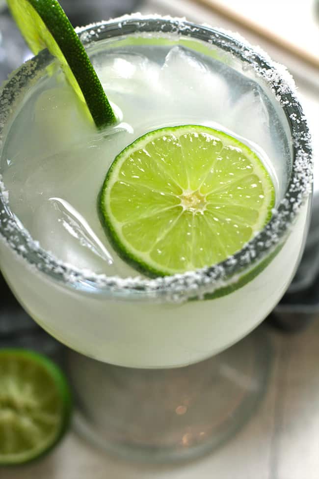 Overhead closeup shot of a classic skinny margarita, with a salt rim and some lime slices.