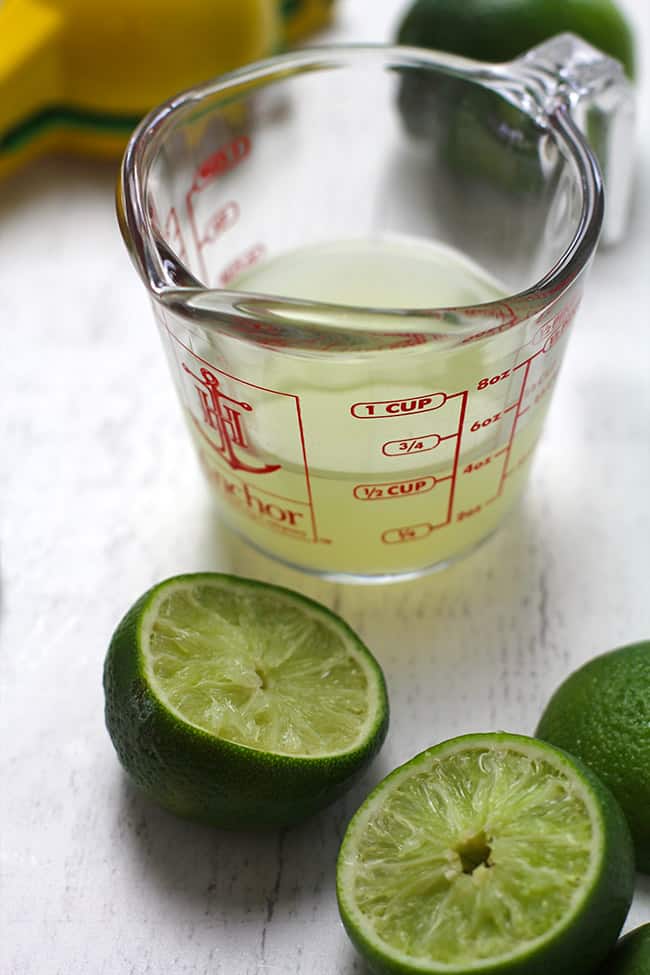 Side shot of a measuring cup filled with 4 ounces of fresh lime juice, on a white background.