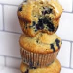 Side shot of a stack of three blueberry muffins, against a white background.