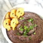 A white bowl of chilled black bean dip, with some pretzel crisps inside, topped with cilantro.