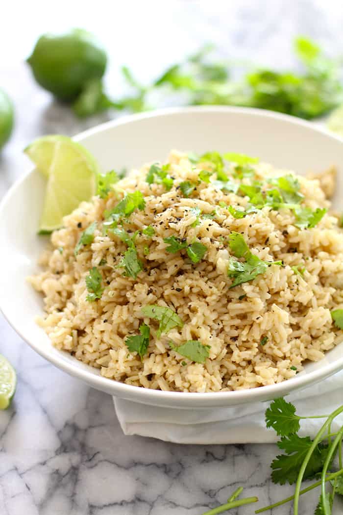 Cilantro lime rice in a white bowl with lime wedges.