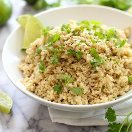 A white bowl filled with cilantro lime rice, wit lime wedges.