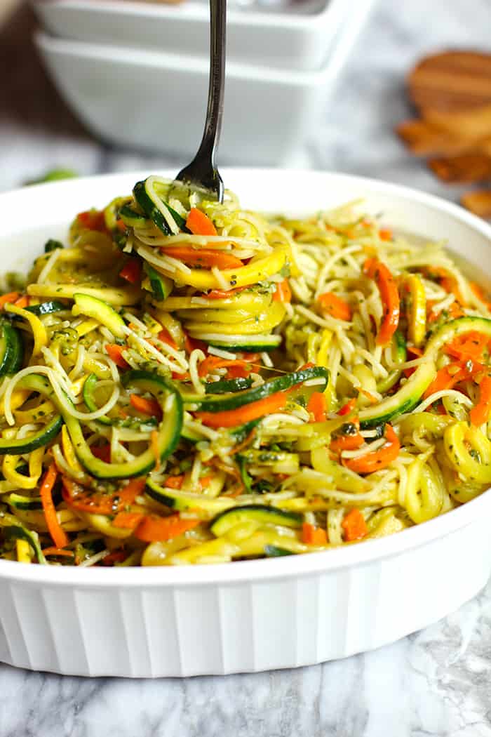 Side angle of vegetable pesto pasta in a white bowl, tossed together with a fork twirling some out from above.