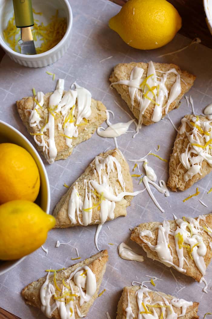 Several lemon scones on some parchment paper, with lemons beside it.