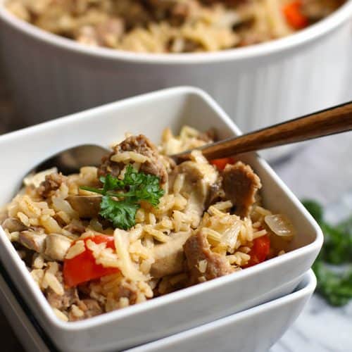 Side shot of a square serving bowl of turkey sausage brown rice, with a fork inside.