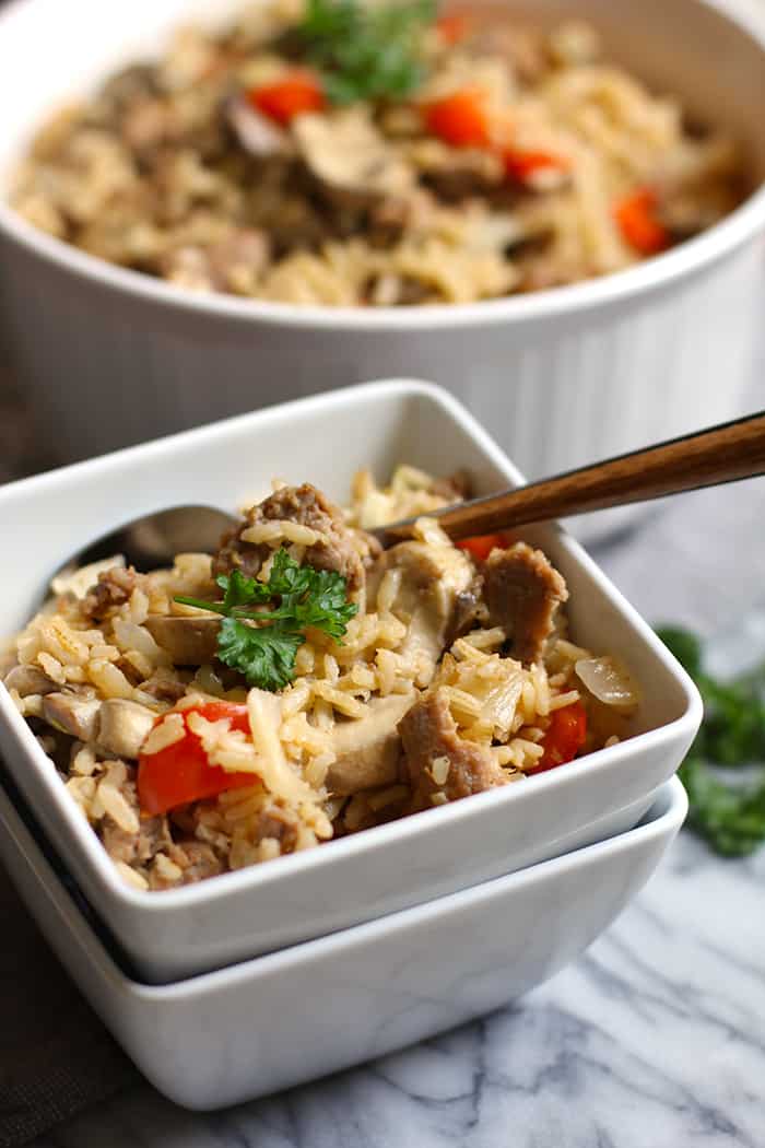 Side shot of a square serving bowl of turkey sausage brown rice, with a fork inside.