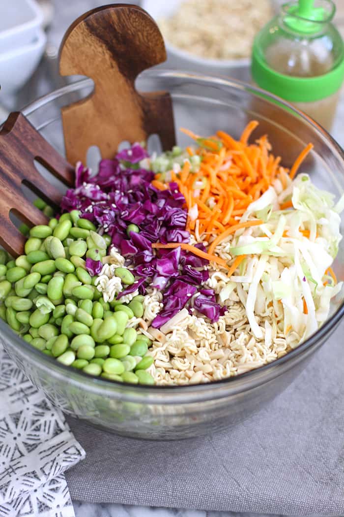 Overhead shot of my Crunchy Asian Cabbage Salad, in a glass bowl, with wooden spoons, on a gray napkin.