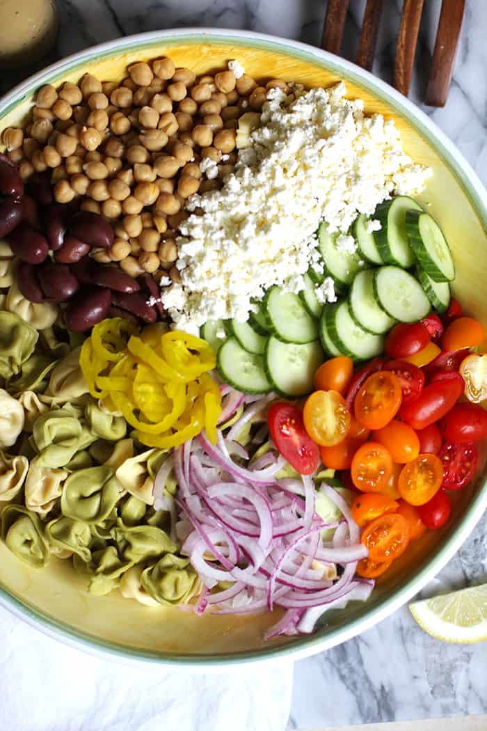 A large bowl of tortellini pasta salad ingredients, separated by ingredient.