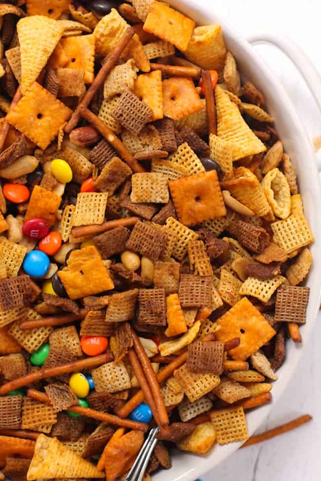 Overhead shot of a partial bowl of spicy Chex party mix, in a white shallow bowl with handles.