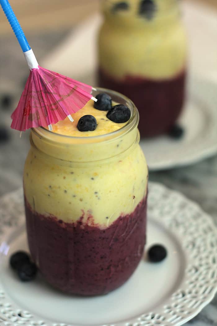 Close-up shot of a blueberry mango smoothie, with a little umbrella straw, on a white plate.