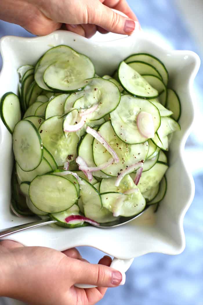 Two hands holding a bowl of fresh cucumbers.