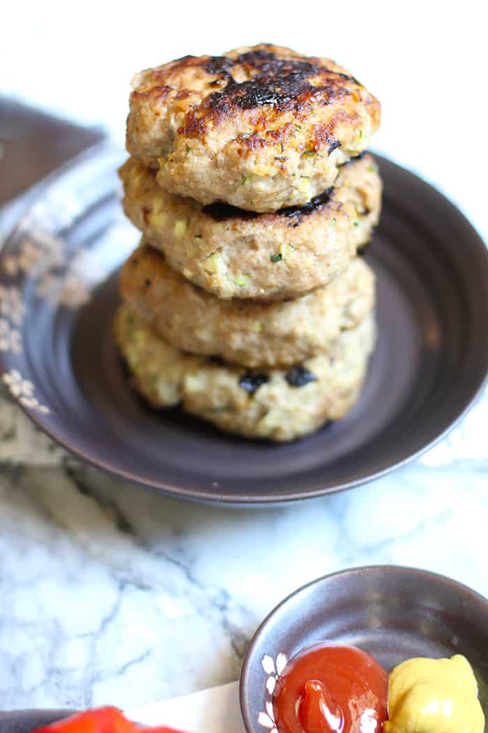 A stack of four grilled zucchini turkey burgers on a plate.